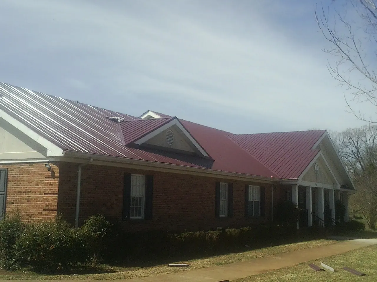 Red metal roof with gabled entries on a long brick building, from a Hail Damage Roof Repair job in Tupelo