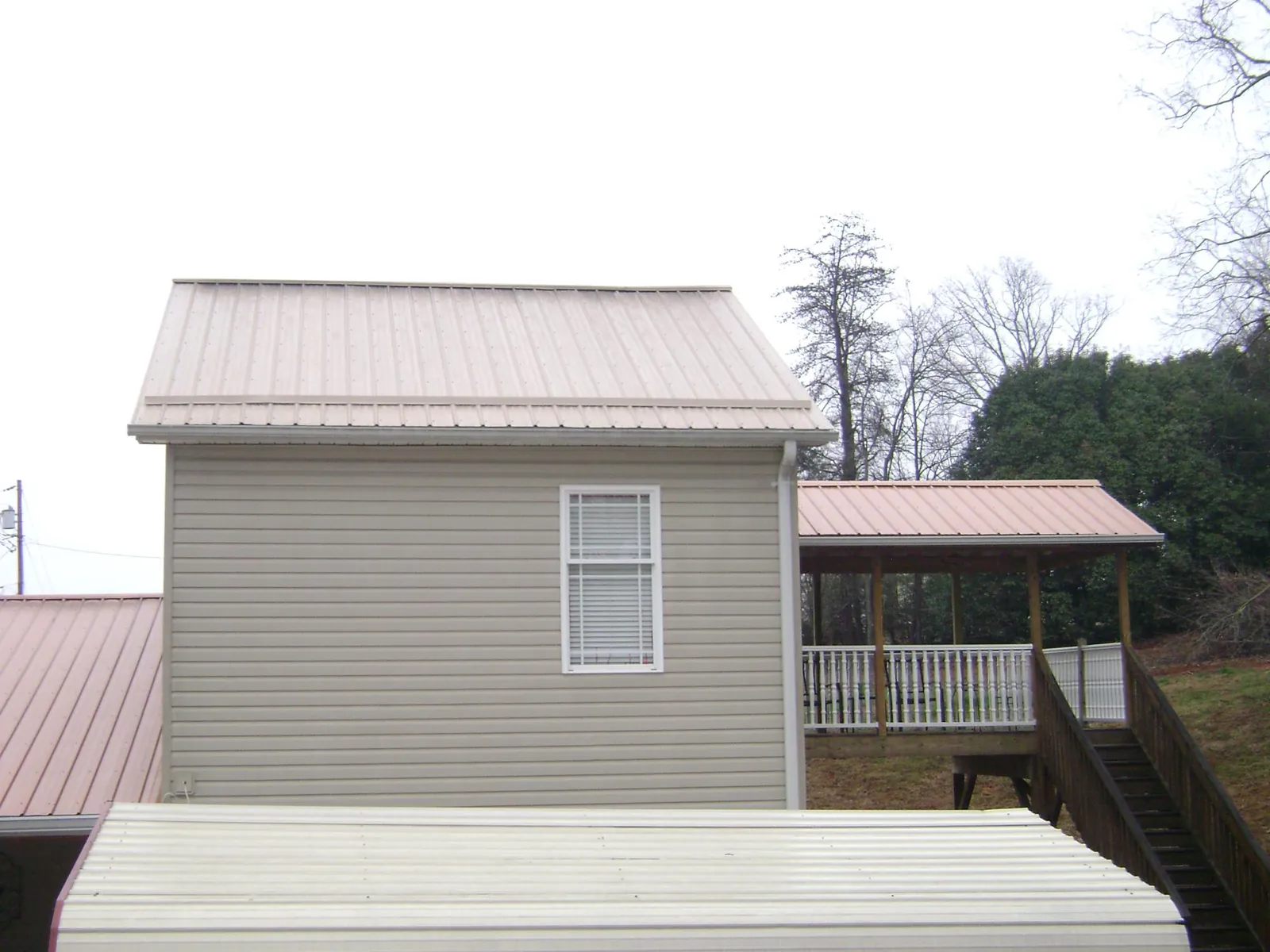 Tan metal roofs on a two story addition and attached porch, from a Roof Replacement job in Tupelo