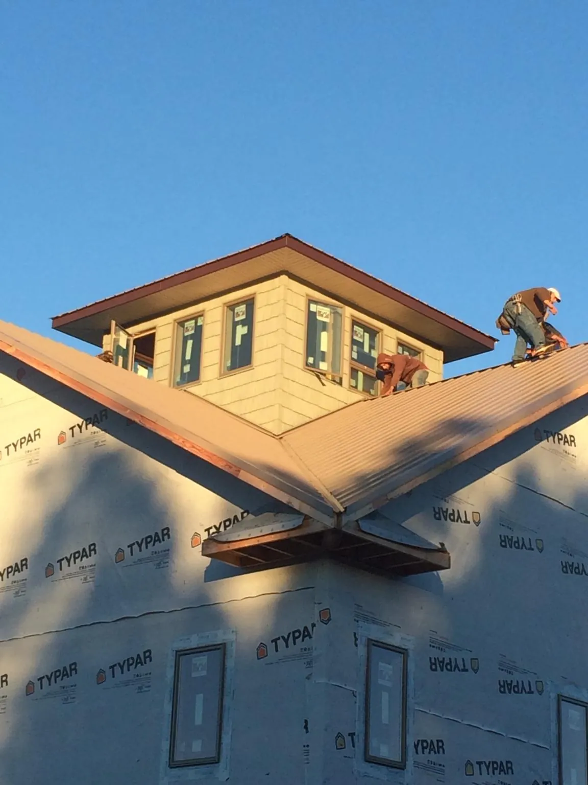 Roofers working around a rooftop cupola on a new metal roof at sunset — Roof Waterproofing in Tupelo by Roofing Brothers